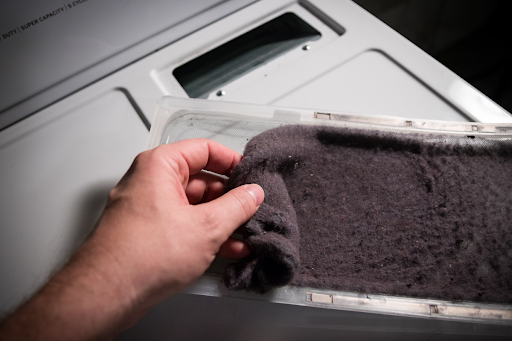 A hand is shown removing the lint build-up in a dryer's lint screen.